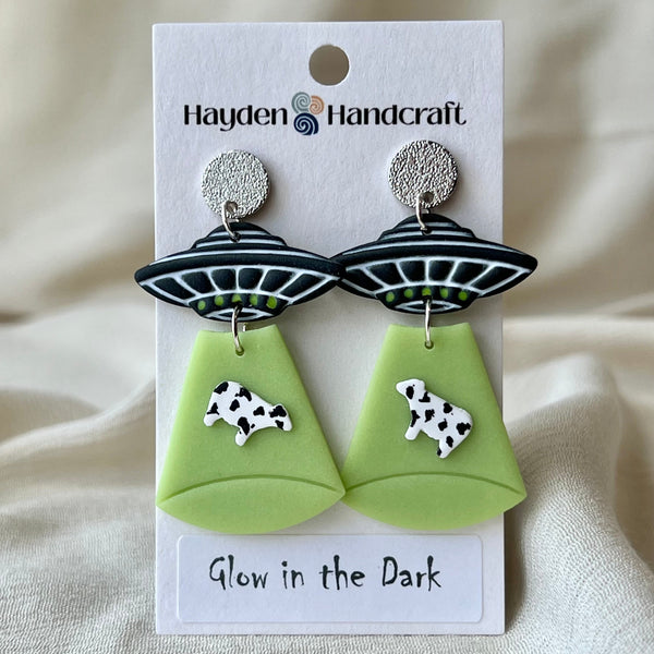 Glow-in-the-dark UFO earrings with cow designs on a Hayden Handcraft card.